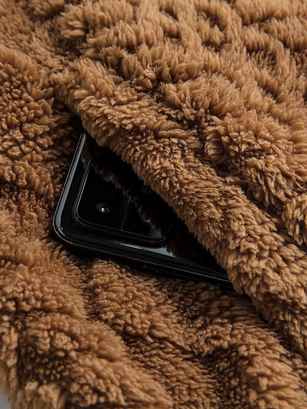 Chaqueta teddy marrón con bolsillo interior; se aprecia un teléfono dentro