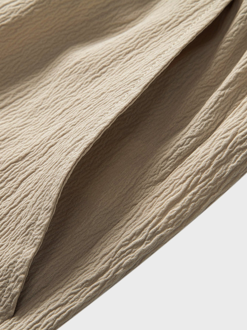Detalle de tela texturizada beige del pantalón, caída y costuras visibles.
