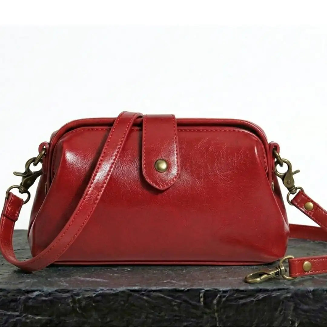 Bolso bandolera vintage de cuero rojo con placa central y correa cruzada.