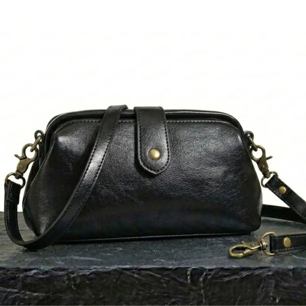 Bolso bandolera vintage de cuero negro con correa ajustable y herrajes dorados.