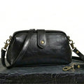 Bolso bandolera vintage de cuero negro con correa ajustable y herrajes dorados.