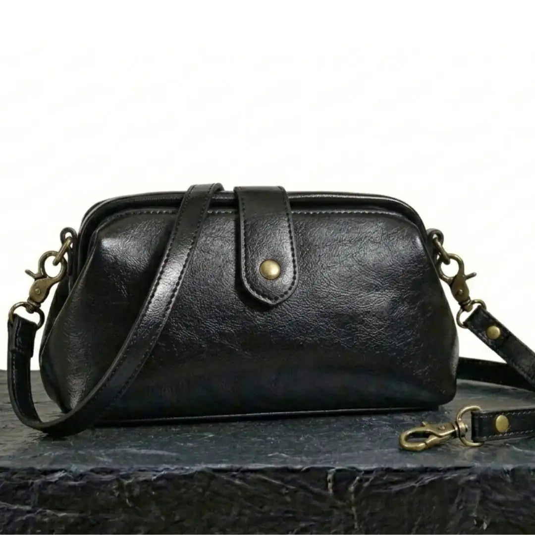 Bolso bandolera vintage de cuero negro con correa ajustable y herrajes dorados.