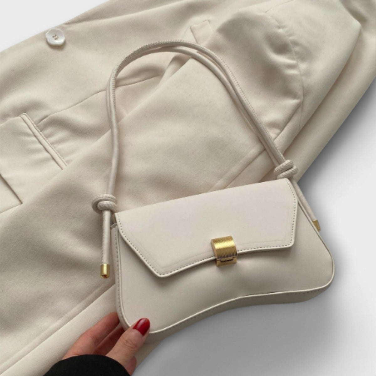 Bolso mini crema con solapa y hebilla dorada; cierre tipo broche rectangular.
