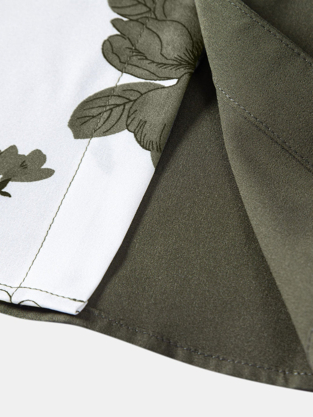 Borde de camisa verde oscuro con costura y estampado floral sobre fondo blanco