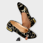 Bailarinas Amélie negras con estampado dorado; tacón ancho bajo y punta redondeada