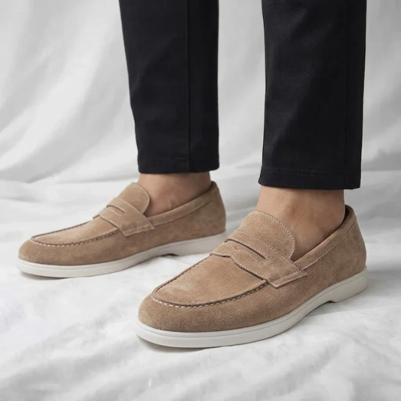 Mocasín de hombre de ante color marrón claro, con tira cruzada y suela blanca.