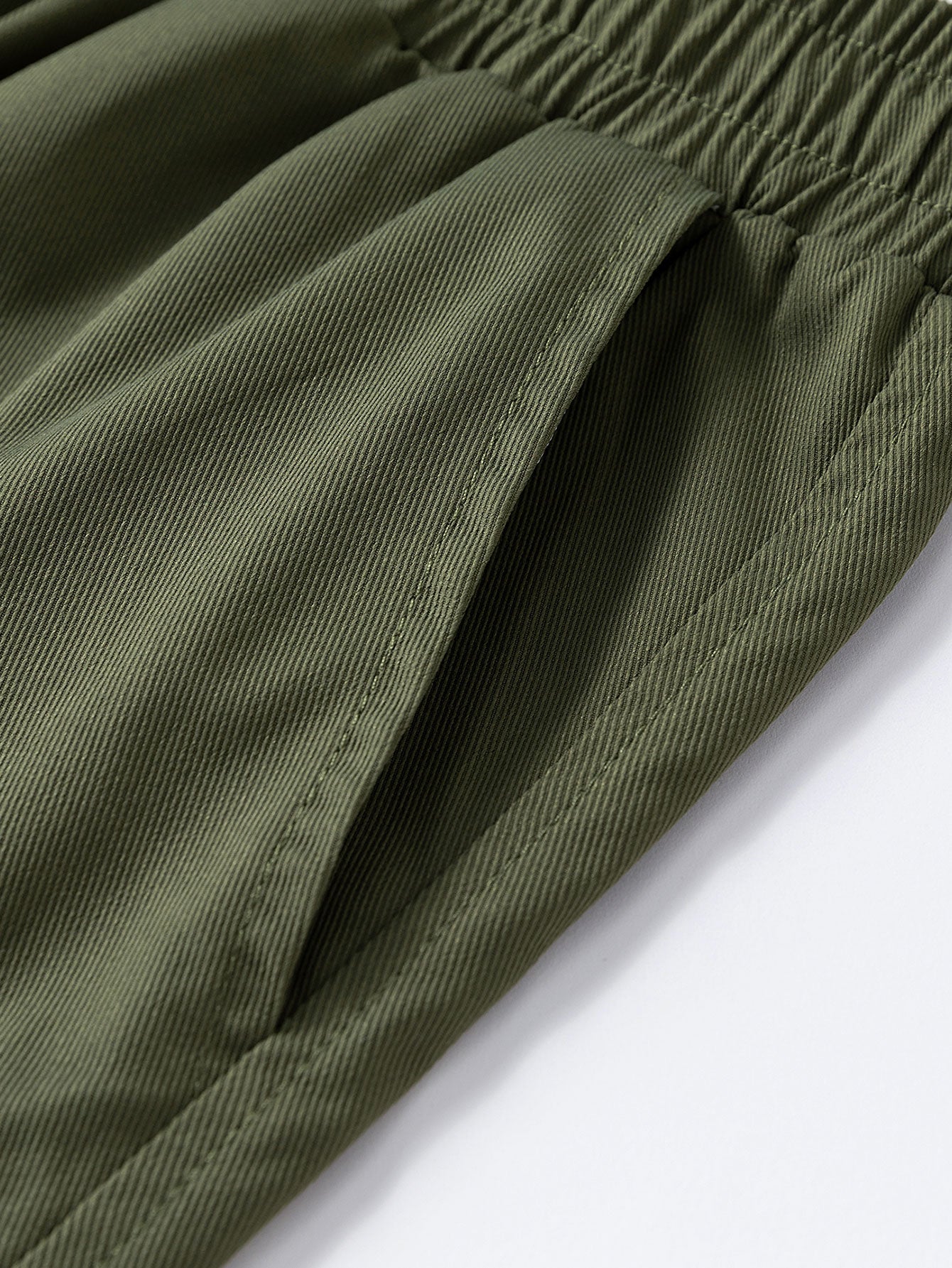 Pantalón corto verde oscuro de tela: costuras visibles en la pierna y dobladillo.