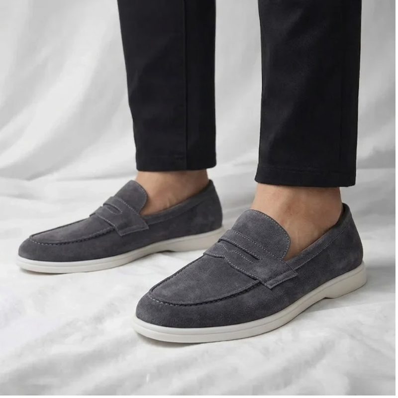 Mocasín de hombre de ante gris oscuro, con tira cruzada y suela blanca.