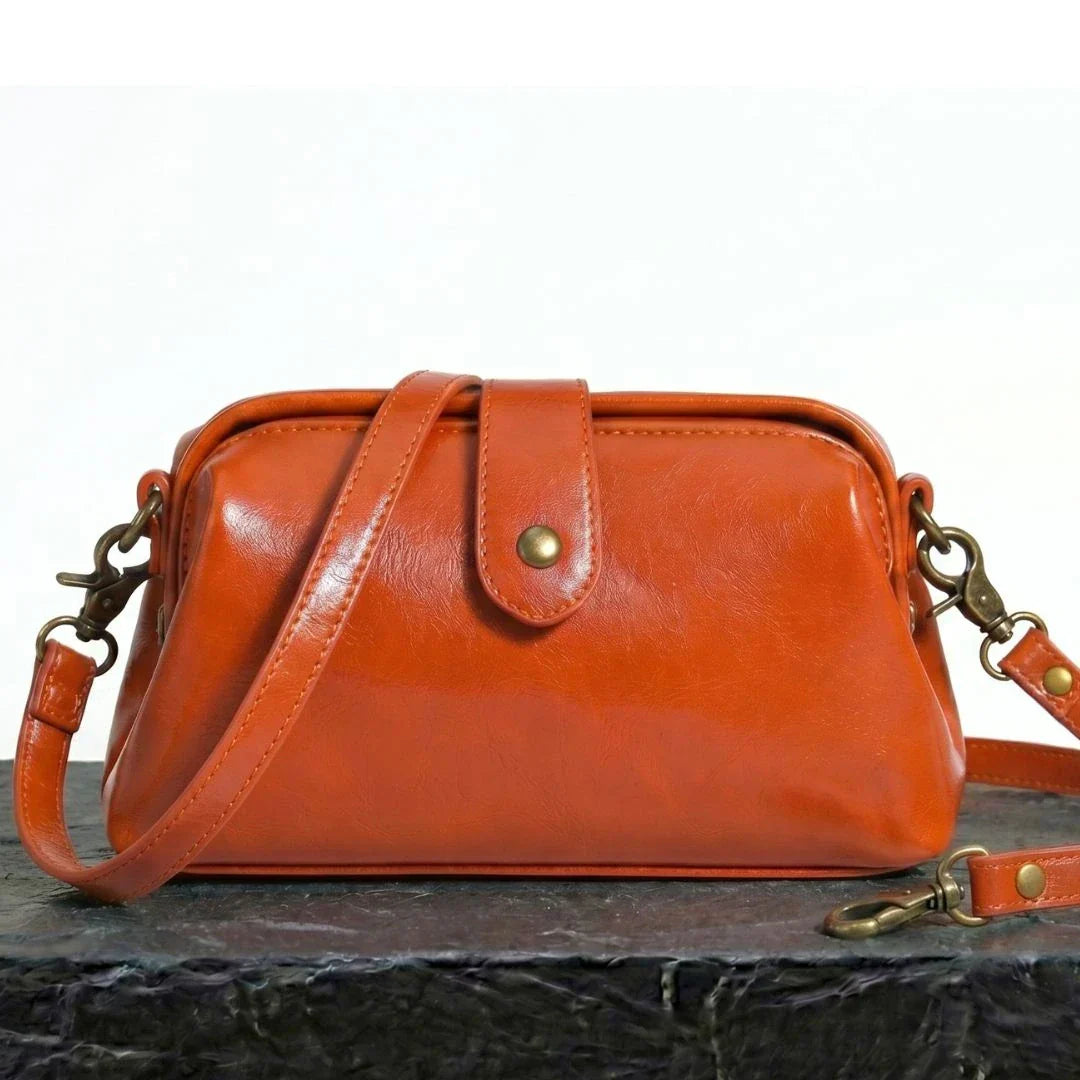 Bolso bandolera vintage de cuero naranja con placa central y correa ajustable.