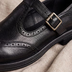 Mocasín Louisa™ de cuero negro con perforaciones y hebilla metálica, detalle