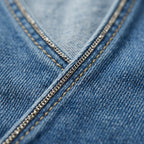Detalle de costura en denim azul con cadena metálica decorativa