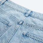 Vaqueros de denim azul claro con costuras y botón; bordado oscuro en el panel frontal