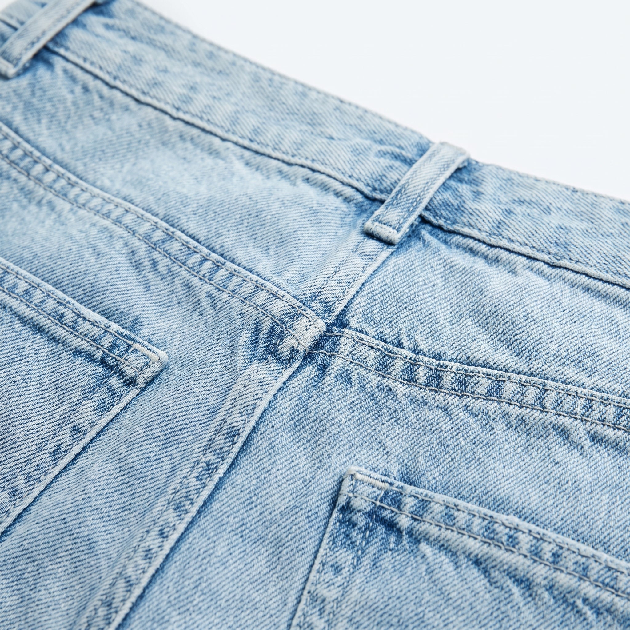 Vaqueros de denim azul claro con costuras y botón; bordado oscuro en el panel frontal