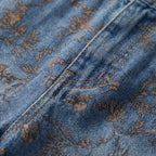 Vaqueros de campana con estampado floral marrón sobre denim azul, costuras visibles