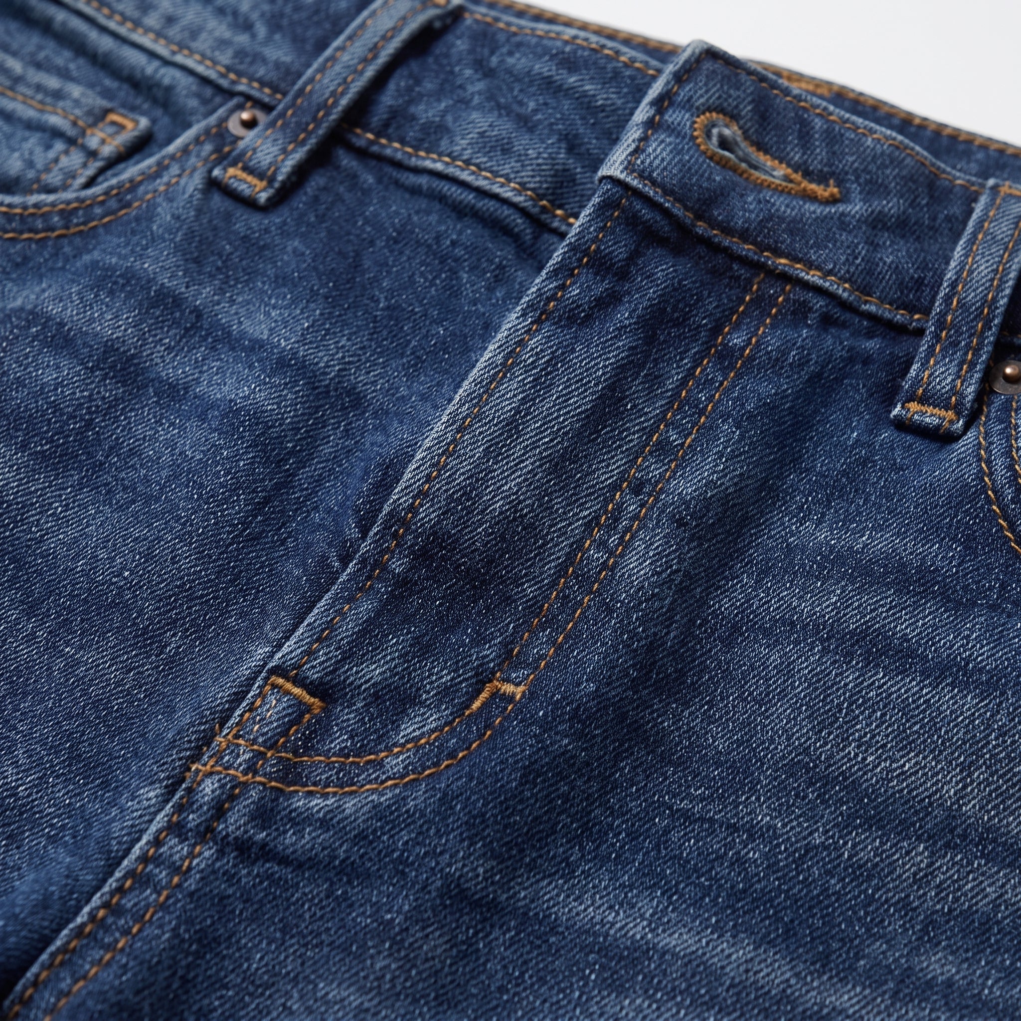 Detalle de vaquero azul oscuro con pespuntes naranjas y costuras en la pierna