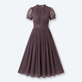 Vestido Lumière viola con encaje floral en cuello y mangas, falda plisada.