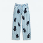 Vaqueros de denim azul claro con apliques negros tipo flor en toda la pierna