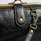 Bolso de cuero negro con etiqueta 'HERITAGE' en solapa y mosquetones metálicos dorados