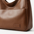 Bolso de piel marrón con etiqueta rectangular cosida en el panel frontal.