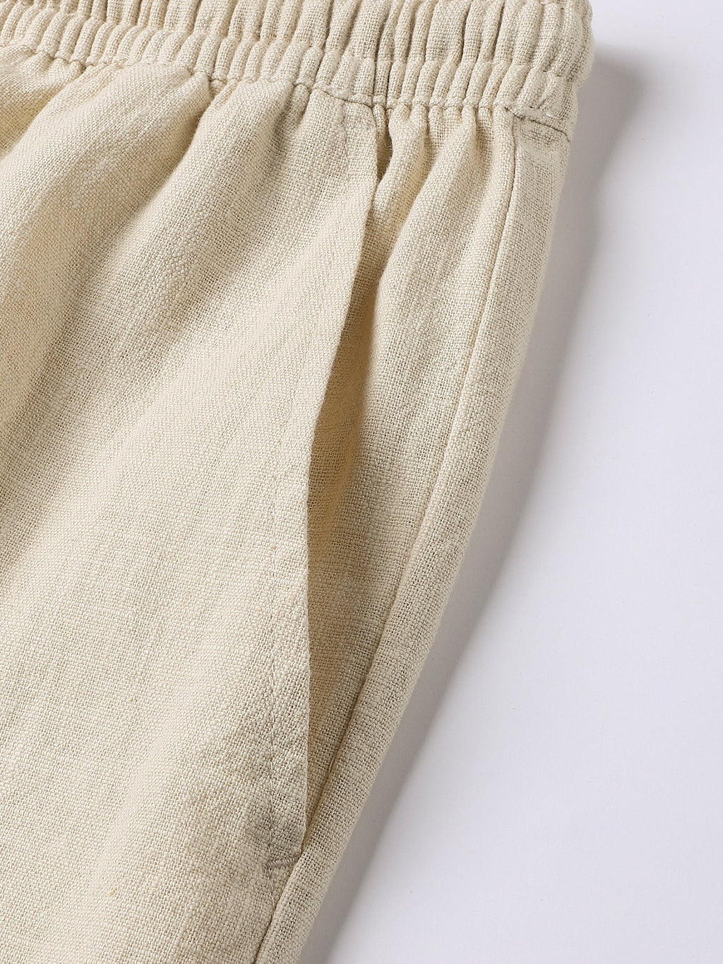 Pantalón corto de lino beige, costuras laterales y caída recta, con cordón visible.