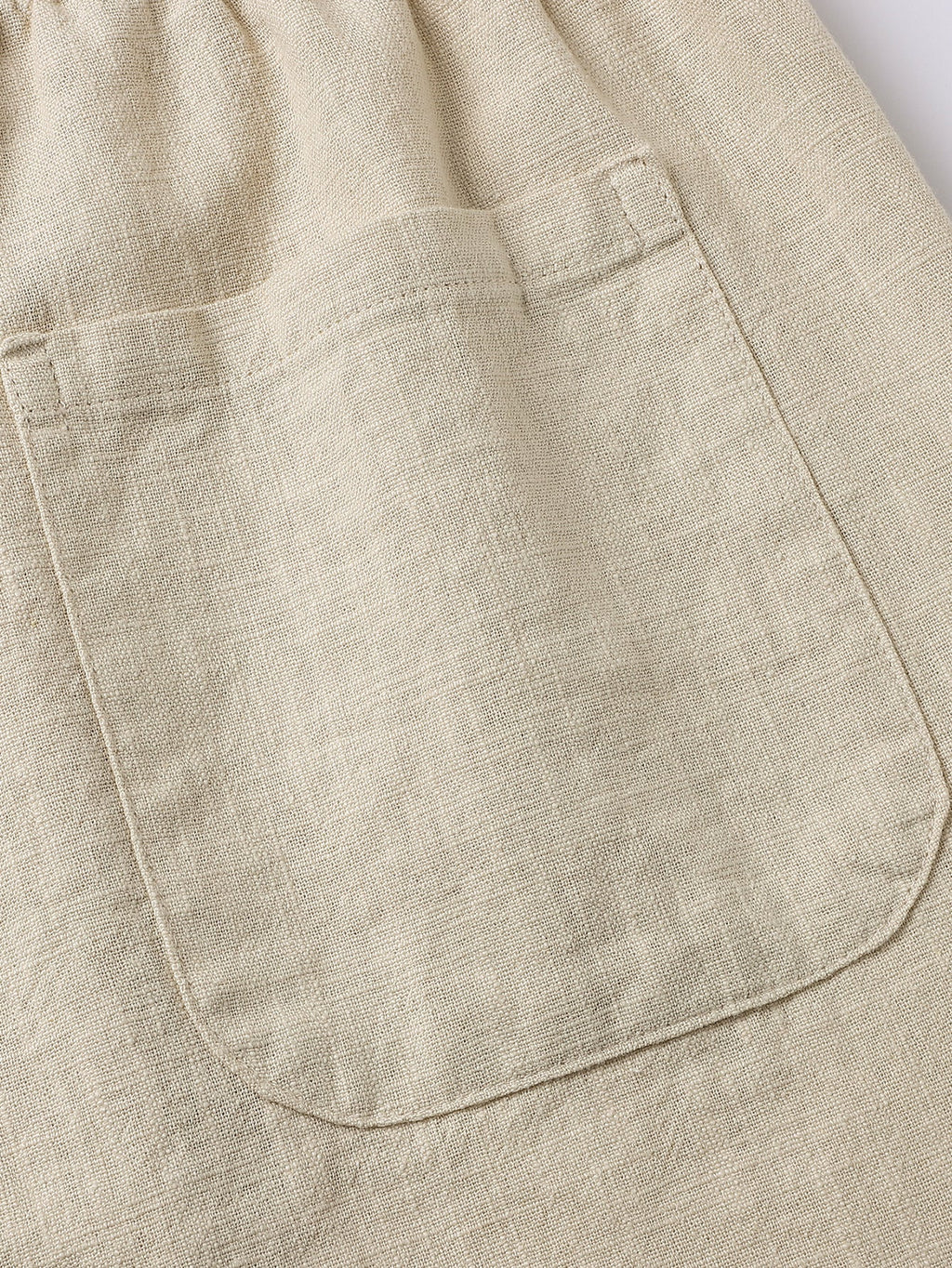 Pantalón corto de lino beige con bolsillo delantero y costuras visibles.