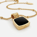 Collar de metal dorado con colgante cuadrado negro y cadena tipo eslabones