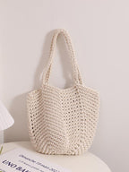 Bolso tote de tejido de rafia, color crudo, asas de cuerda y forma redondeada.