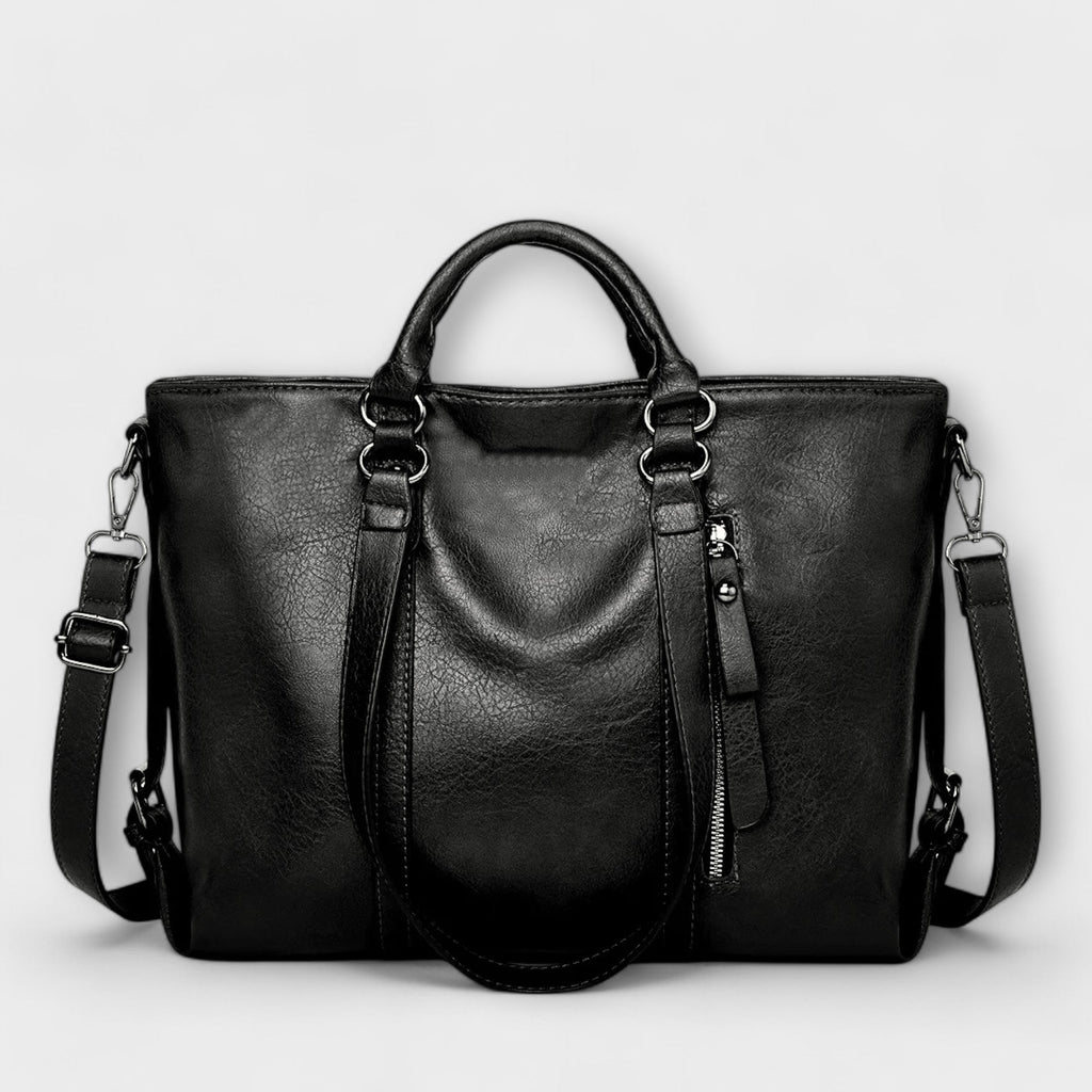 Bolso negro de piel con doble asa, cremallera central y correa ajustable cruzada.