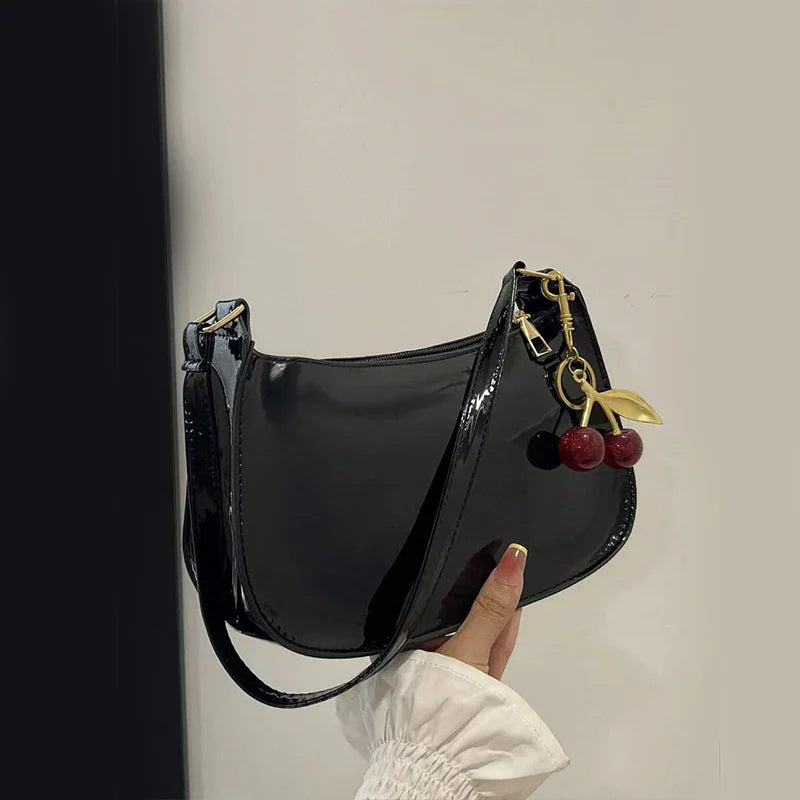 Bolso bandolera de charol negro con correa y llavero con cuentas rojas.