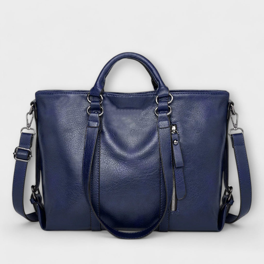 Bolso azul marino de piel con doble asa, cremallera central y correa ajustable cruzada.