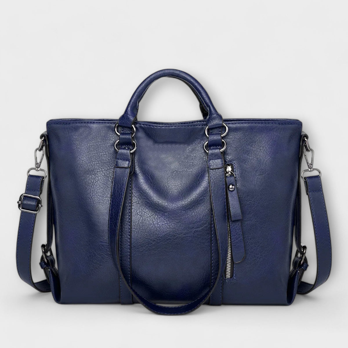 Bolso azul marino de piel con doble asa, cremallera central y correa ajustable cruzada.