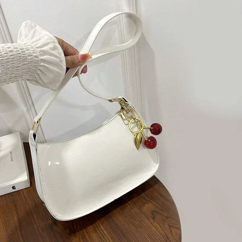 Bolso bandolera de charol blanco con correa y llavero metálico con cuentas rojas.
