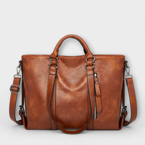 Bolso marrón de piel con doble asa, cremallera central y correa ajustable cruzada.
