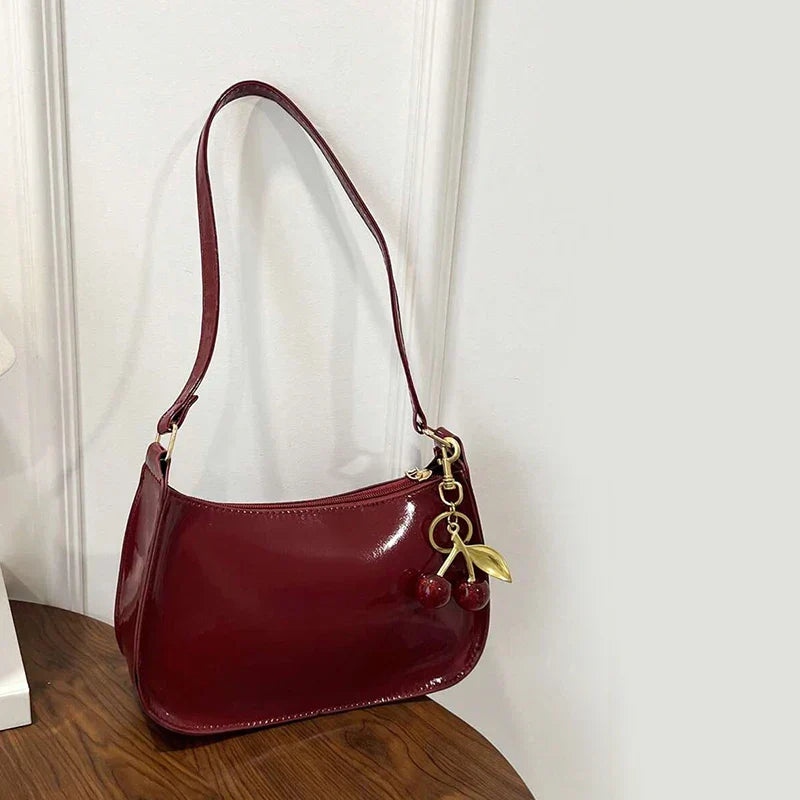 Bolso bandolera de charol granate con correa larga y colgante metálico y cuentas.