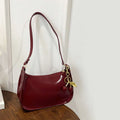 Bolso bandolera de charol granate con correa larga y colgante metálico y cuentas.