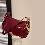 Bolso bandolera de charol granate con correa ajustable y llavero de cuentas rojas.