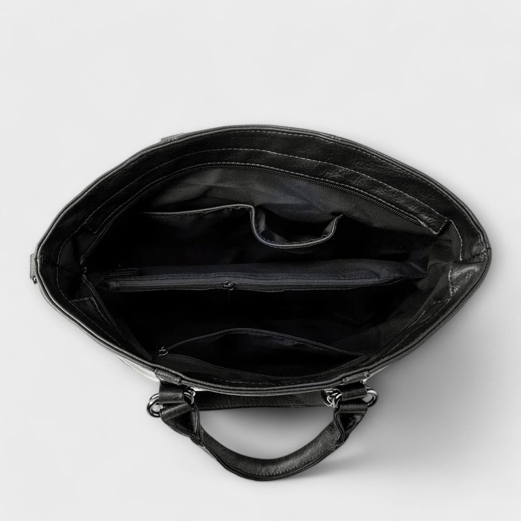 Bolso negro abierto, interior forrado con compartimentos y cremallera superior.