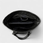 Bolso negro abierto, interior forrado con compartimentos y cremallera superior.