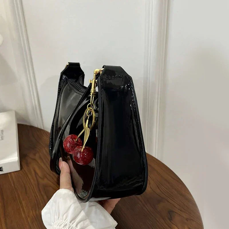 Bolso bandolera de charol negro con correa y llavero metálico con cuentas rojas.