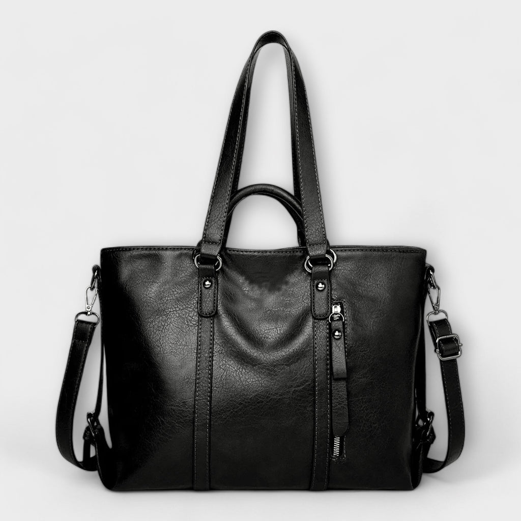 Bolso negro de piel con doble asa, cremallera decorativa y correa cruzada con mosquetones.