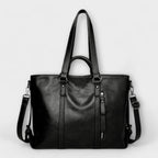 Bolso negro de piel con doble asa, cremallera decorativa y correa cruzada con mosquetones.