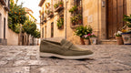Mocasín de hombre de ante verde oscuro, con tira cruzada y suela blanca.