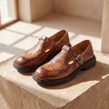 Mocasín Louisa™ de cuero marrón con hebilla, par sobre escalón de piedra