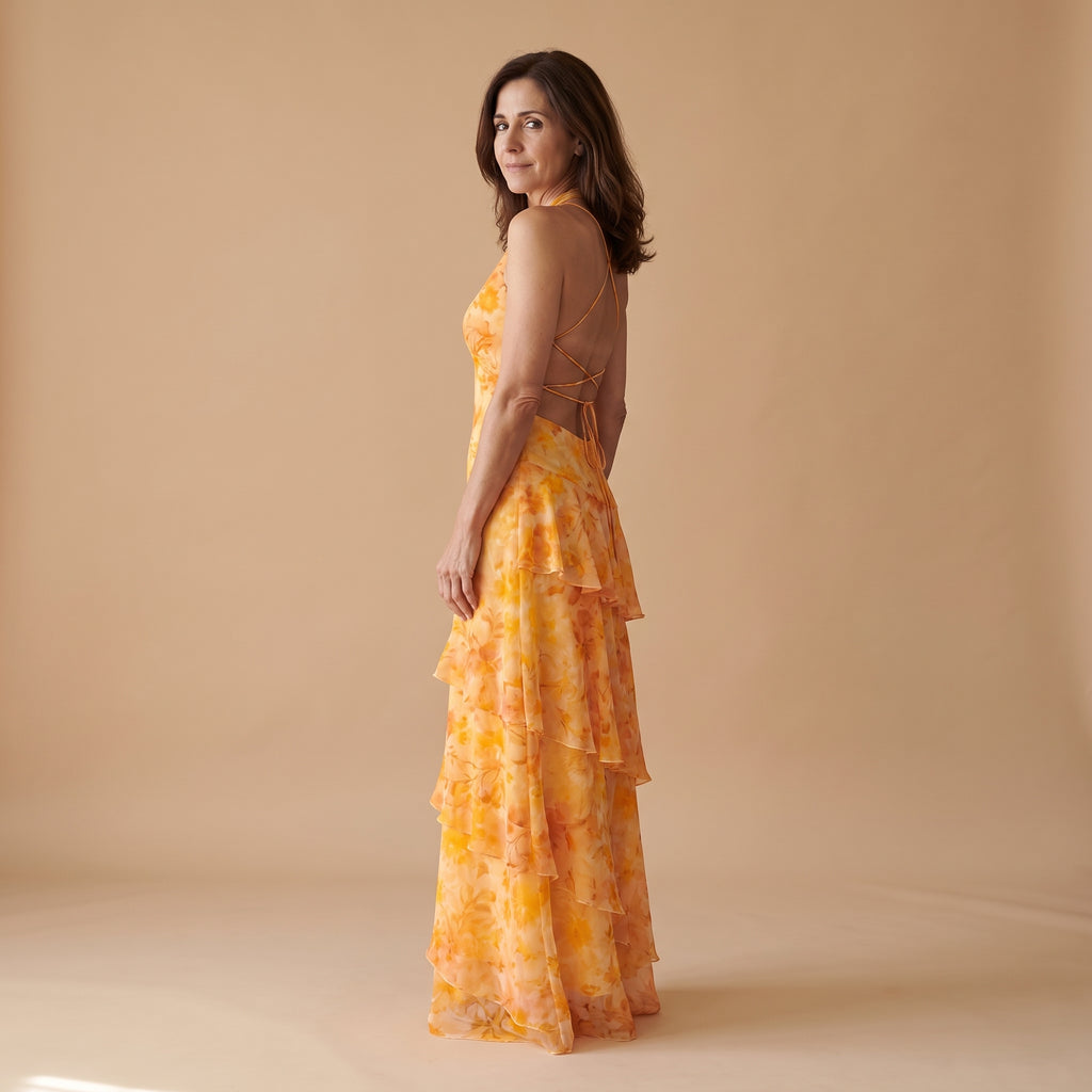 Vestido largo dorado con estampado floral, espalda con tiras cruzadas y falda con volantes