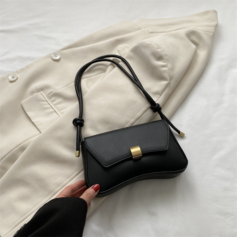Bolso mini negro con solapa y hebilla dorada, asas trenzadas y cordones.
