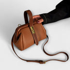Bolso Maelis marrón de piel con asas cortas y correa larga ajustable, herrajes dorados.