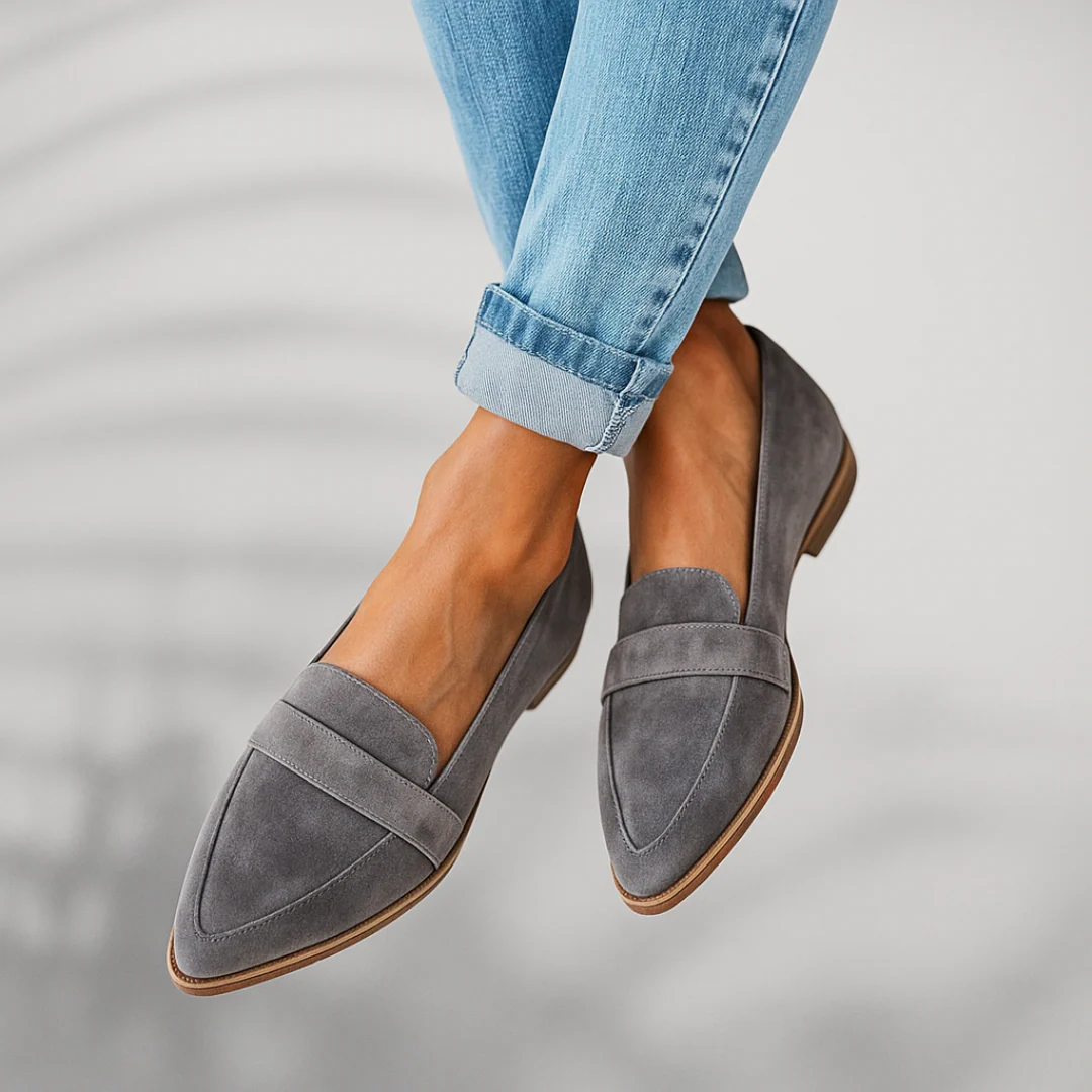 Mocasines de ante color gris con tira al empeine y suela marrón, vista lateral.