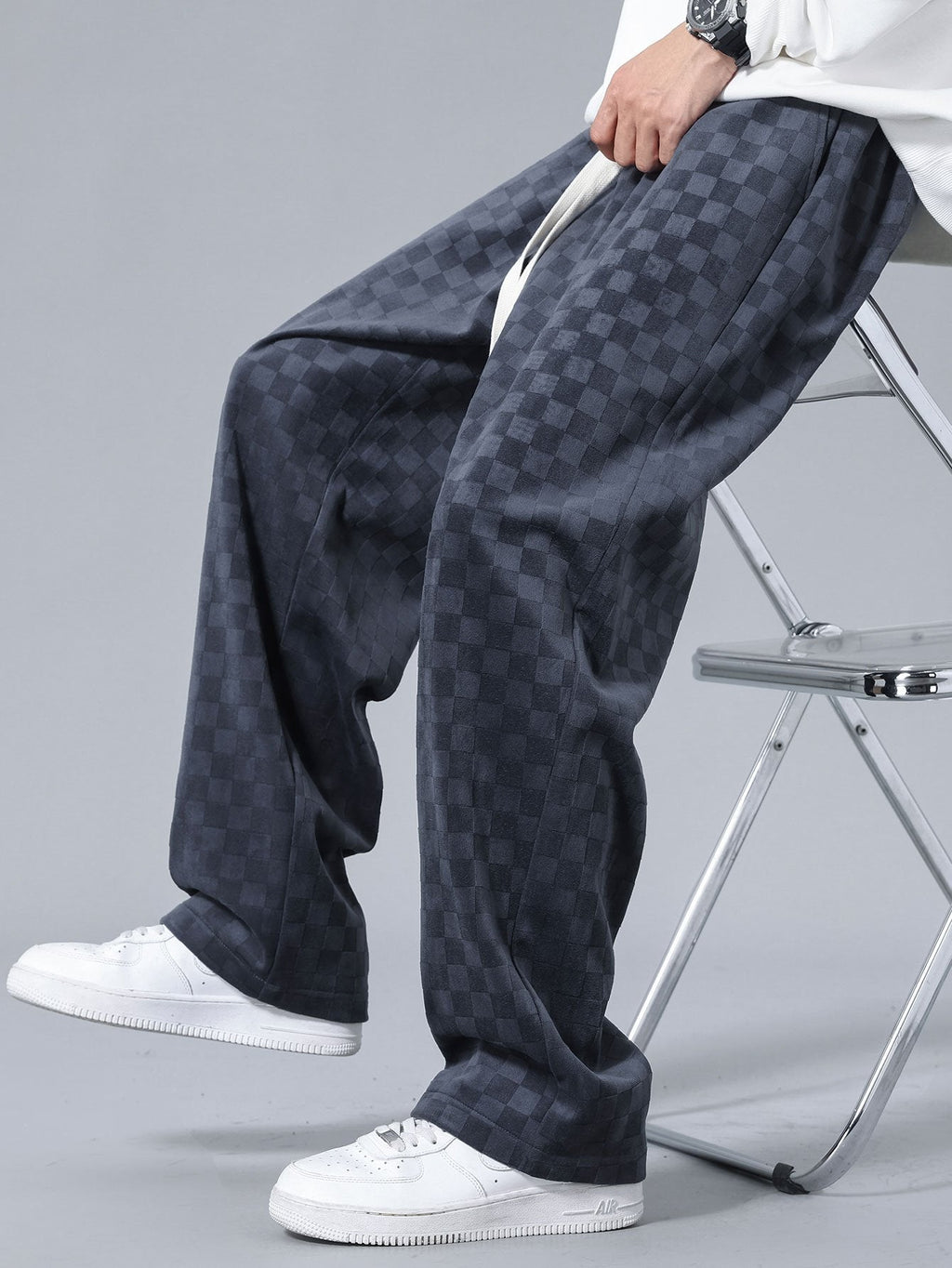 Pantalón recto oscuro con patrón damero, cordón blanco y pliegues en el tejido.