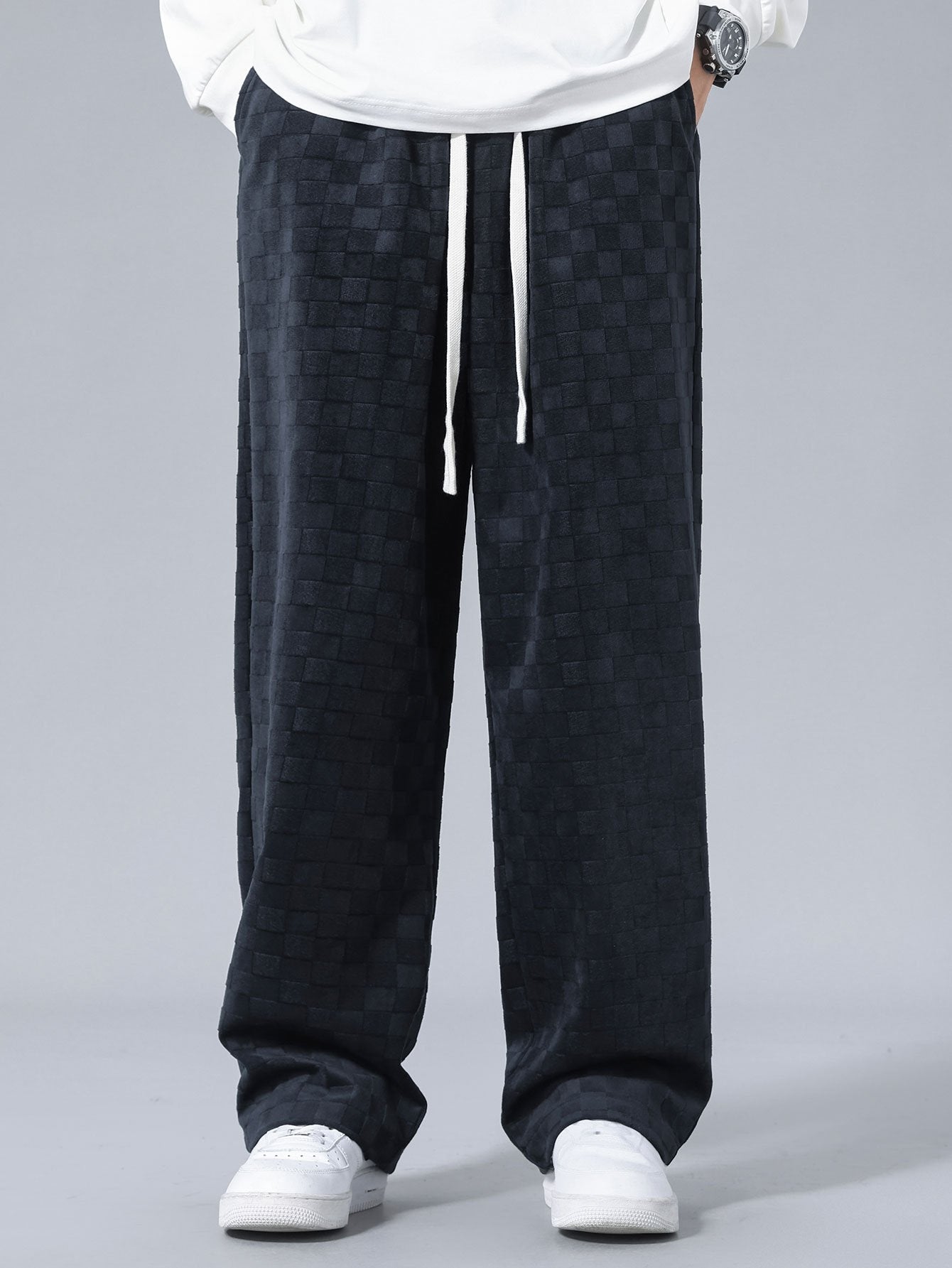 Pantalón recto oscuro con patrón damero, cordón blanco y pierna ancha.