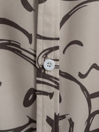 Botón frontal de camisa color arena con estampado oscuro y costuras visibles